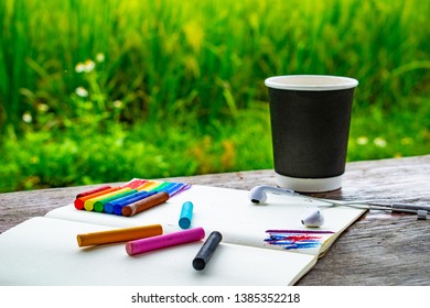 Draw Rainbow By Chalks On Notebook, Earphones In The Park, Green Grass And Wooden Structure Table Art Style, Cold Design And Cold Colours