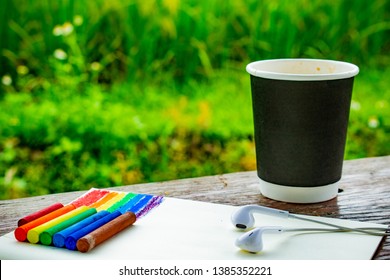 Draw Rainbow By Chalks On Notebook, Earphones In The Park, Green Grass And Wooden Structure Table Art Style, Cold Design And Cold Colours