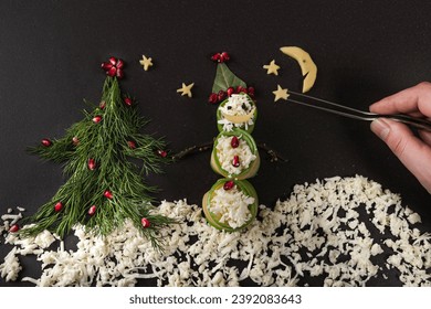 Drawing with food.  The concept of the Christmas and  New Year holiday. Flat lay. A snowman made of cucumbers and cheese, a Christmas tree made of dill, pomegranate seeds, a moon made of cheese. - Powered by Shutterstock