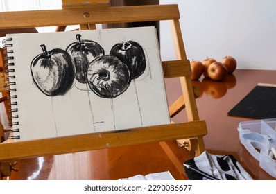 Drawing fruit with charcoal, four apples, on a sketch pad on a portable easel