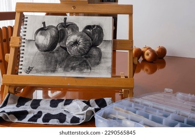 Drawing fruit with charcoal, four apples, on a sketch pad on a portable easel