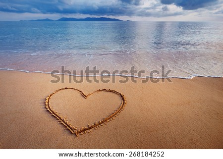 A drawing of a heart on a yellow sand at a beautiful seascape background.