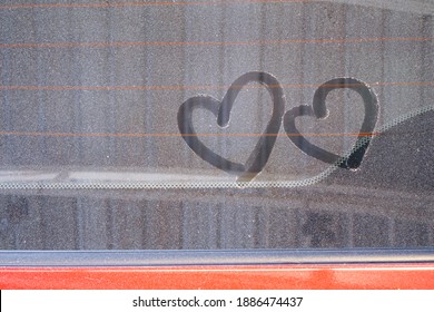 drawing heart shape on dirty and dusty red car rear windscreen or window , valentine for car lover and car care concept