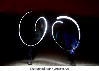 Drawing With Light At Night With Long Exposure. Spiral Circles And Wavy Lines Using Pyrotechnic Sparklers Led Lights. White Color Effect Hand Movements Of Children, Lightsabers, Sabre