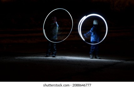 Drawing With Light At Night With Long Exposure. Spiral Circles And Wavy Lines Using Pyrotechnic Sparklers Led Lights. White Color Effect Hand Movements Of Children, Lightsabers, Sabre