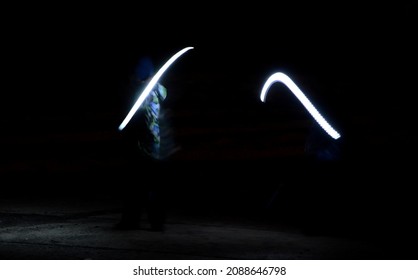 Drawing With Light At Night With Long Exposure. Spiral Circles And Wavy Lines Using Pyrotechnic Sparklers Led Lights. White Color Effect Hand Movements Of Children, Lightsabers, Sabre