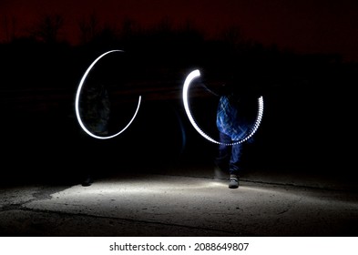 Drawing With Light At Night With Long Exposure. Spiral Circles And Wavy Lines Using Pyrotechnic Sparklers Led Lights. White Color Effect Hand Movements Of Children, Lightsabers, Fencing