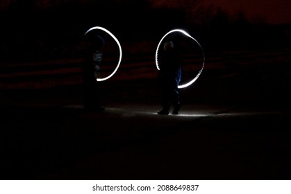 Drawing With Light At Night With Long Exposure. Spiral Circles And Wavy Lines Using Pyrotechnic Sparklers Led Lights. White Color Effect Hand Movements Of Children, Lightsabers, Fencing