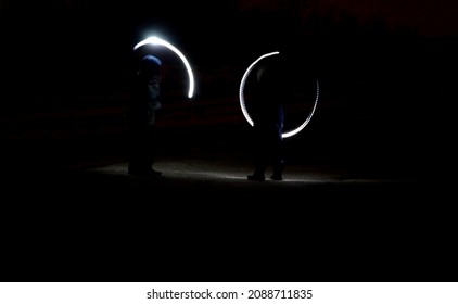 Drawing With Light At Night With Long Exposure. Spiral Circles And Wavy Lines Using Pyrotechnic Sparklers Led Lights. White Color Effect Hand Movements Of Children, Lightsabers, Fencing