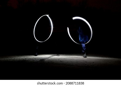 Drawing With Light At Night With Long Exposure. Spiral Circles And Wavy Lines Using Pyrotechnic Sparklers Led Lights. White Color Effect Hand Movements Of Children, Lightsabers, Fencing