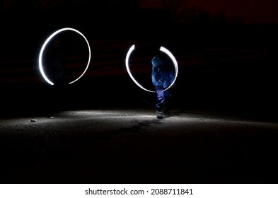 Drawing With Light At Night With Long Exposure. Spiral Circles And Wavy Lines Using Pyrotechnic Sparklers Led Lights. White Color Effect Hand Movements Of Children, Lightsabers, Fencing