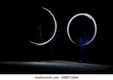 Drawing With Light At Night With Long Exposure. Spiral Circles And Wavy Lines Using Pyrotechnic Sparklers Led Lights. White Color Effect Hand Movements Of Children, Lightsabers, Fencing