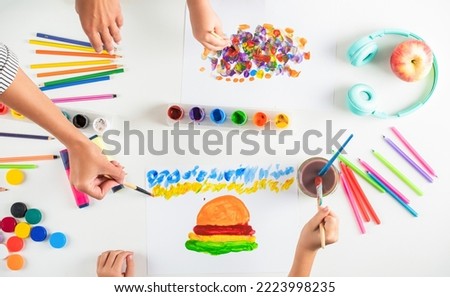 Drawing on a white sheet of paper. Creativity and art. Hands paint brush. Kid hands painting at the table with art supplies. Hands with brush painting with watercolor abstract stains.