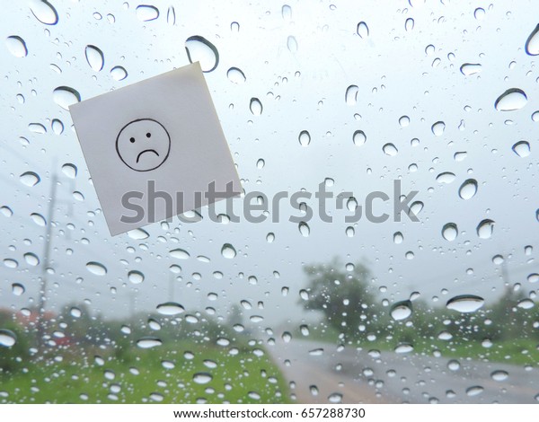 drawing of sad face on sticky\
note paper on the windshield with rain drop background outside.    \
  