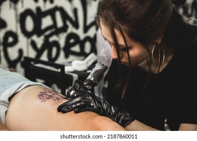 Drawing Of A Tattoo On The Leg Close-up. Woman Tattoo Artist Makes A Drawing With A Special Machine In An Art Studio