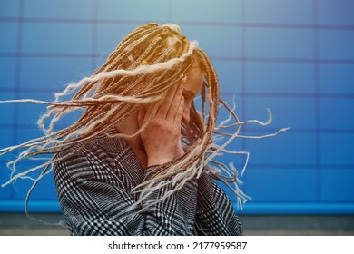 Dreads shaking lighthearted teenage girl in front of a blue panel wall covering. She is wearing a grey checkered jacket. Portrait. - Shutterstock ID 2177959587
