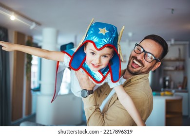 Dream Big. Loving Father Helps His Son Fly Like A Superhero. Boy Play Fly With His Dad At Home. Cheerful Familyare Having Fun Together. Father Holding Son In Superhero Costume Flying At Home 