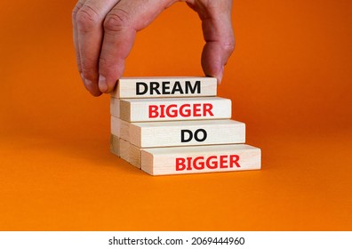 Dream And Do Bigger Symbol. Concept Words 'Dream Bigger Do Bigger' On Wooden Blocks On A Beautiful Orange Background. Businessman Hand. Business, Motivational And Dream And Do Bigger Concept.