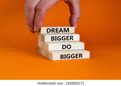 Dream And Do Bigger Symbol. Concept Words 'Dream Bigger Do Bigger' On Wooden Blocks On A Beautiful Orange Background. Businessman Hand. Business, Motivational And Dream And Do Bigger Concept.