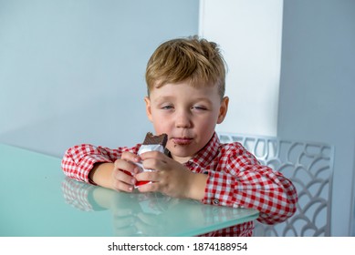 Dream Interpretation Little Boy Eats A Chocolate Bar In The Kitchen. Boy Sits At The Table And Eats A Chocolate Bar. 