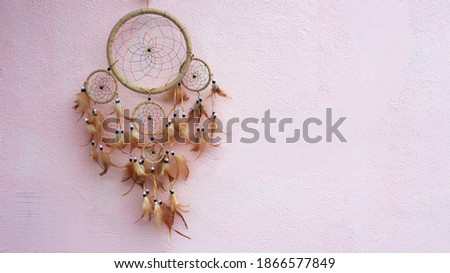 Dreamcatcher on a pink background. Place for text. Selective focus. Handmade dreamcatcher with thread feathers and hanging rope beads.