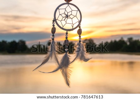 Dreamcatcher at sunset time in windy day with orange of sky and water reflections in background.