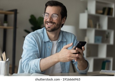 Dreamer. Inspired young man sit at table holding cell look at distance excited with new opportunity offered by business email. Happy motivated millennial male enjoy good news received at phone message