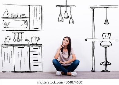 Dreaming about new kitchen. Cheerful young woman smiling while sitting on the floor against white background with drawn kitchen