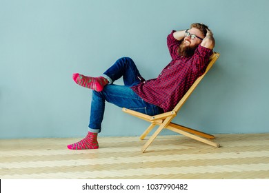 Dreaming about vacation concept. Studo shot of man resting on a chair over gray wall at home.