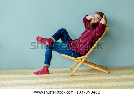 Dreaming about vacation concept. Studo shot of man resting on a chair over gray wall at home.