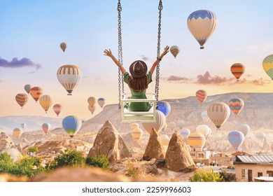 Dreaming woman swinging in Kapadokya. Flying hot air balloons in Anatolia. Happy moment life in beautiful destination in Goreme, Nevsehir 