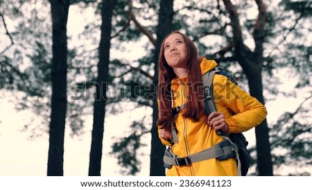 Dreaming woman with tourist backpack walks looking around fir forest slow motion. Woman backpacker contemplates beauty of coniferous wood at hike. Woman enjoys solitude at picturesque woodland