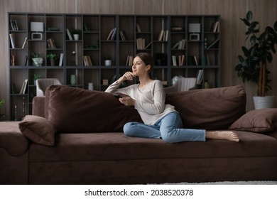 In dreams. Calm peaceful young lady sit on sofa hold cell create plans on free day weekend at comfortable home interior. Thoughtful teen female rest at living room think on good news received by cell