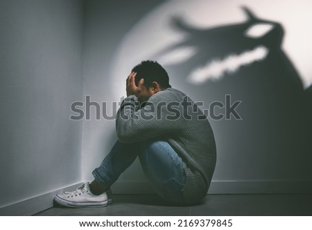 If dreams come true, can nightmares too. Shot of a young man sitting in the corner of a dark room with a scary figure on the wall.