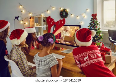 Dreams Come True On Christmas. Children Gathering Together At Home, Looking At Computer Screen During Video Call, Listening To Santa Claus Reading Out Loud Names Of Good Kids From Naughty Or Nice List