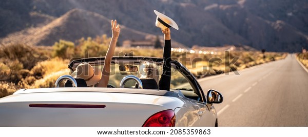 Dreams\
come true! Two happy young girls driving cabrio car during vacation\
road trip in mountains, making memories and having fun together.\
Back view.Freedom concept. Happiness. Tourist.\
