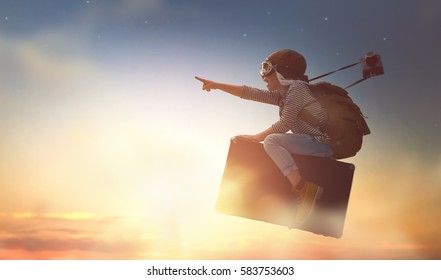 Dreams of travel! Child flying on a suitcase against the backdrop of sunset.