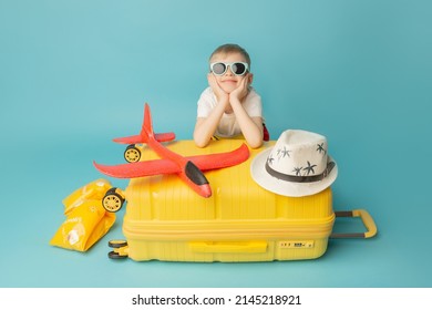 Dreams of travel. Child with a yellow suitcase and beach stuff on the blue background.
