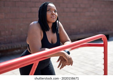 Dreamy Afro American Woman In Black Sportive Clothes Having Rest, Looking At Side In City, In Sports Ground, Relaxing, Thinking, Having Some Minutes To Take A Break During Jogging Or Fitness Workout