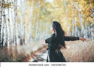 Dreamy beautiful girl with long natural black hair flies on bokeh background of autumn yellow leaves. Autumn euphoria in faded tones. Inspired emotional girl enjoys nature in fall forest. Back view. - Shutterstock ID 1421546714