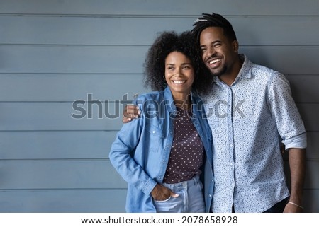 Dreamy bonding affectionate young African American married family couple looking in distance, visualizing or planning common future, posing on grey wall background, copy space for ad text.