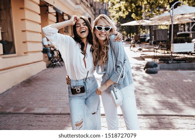 Dreamy caucasian girls posing together on the street. Pleased female friends smiling on city background.