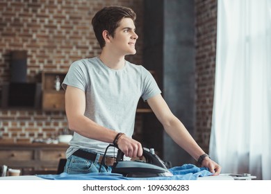 Dreamy Caucasian Teenager Ironing Blue Shirt At Home