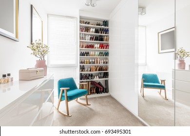 Dreamy feminine wardrobe with white furniture, big mirror, shoe closet, beige carpet, blue retro armchair and pastel pink accessories