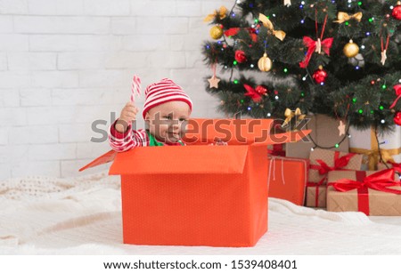 Dreamy gift. Cheerful baby with lollipop sitting in big present box, free space
