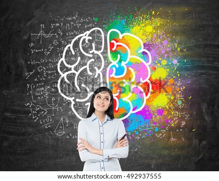 Dreamy girl with black hair standing near blackboard with brain sketches on it. Concept of brain studying