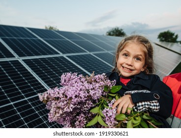 Dreamy girl with a bouquet of flowers on a background of solar panels. Portrait of a smiling child holding lilac flowers in the area near the house. The concept of ecology, a happy future. Happy child - Shutterstock ID 1919330621