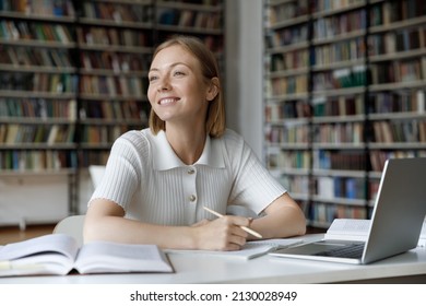 Dreamy Happy Young Beautiful Caucasian Woman Looking In Distance, Distracted From Studying On Online Courses, Reading Educational Books Or Preparing For Exams Alone In Modern College Library.