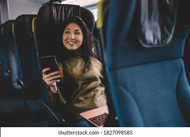 Dreamy happy youthful dark haired Asian female in casual clothes sitting with mobile phone in bus while thinking and looking away - Powered by Shutterstock