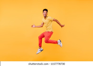 Dreamy male model. Indoor shot of african guy in bright clothes jumping on yellow background.